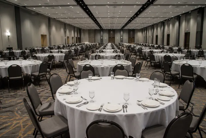 A hotel banquet hall with upholstered chairs around fully set round tables